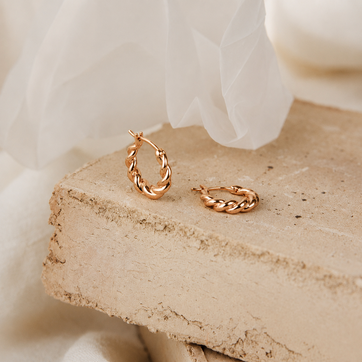 Gold hoop earrings on a textured stone surface with a soft white fabric background
